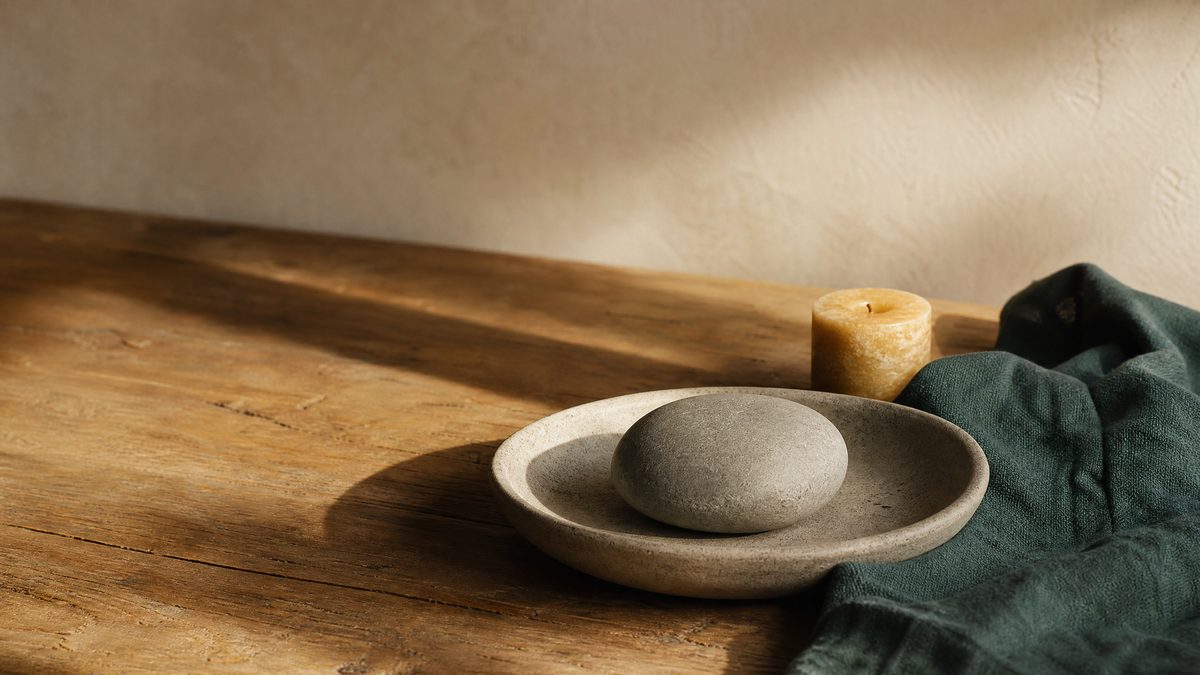 Smooth stone resting in a shallow ceramic dish casting a long shadow, representing the weight of guilt and conscience